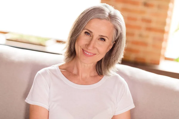 Photo of pretty adorable smiling lady pensioner wear white t-shirt sitting couch smiling indoors house flat — ストック写真