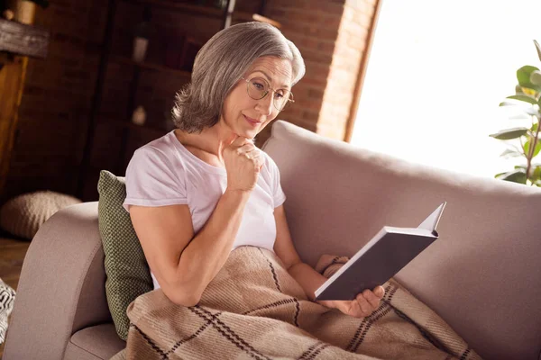 Portrait of attractive grey-haired woman sitting on sofa reading book daydream vacation at home house indoors modern brick loft interior — ストック写真