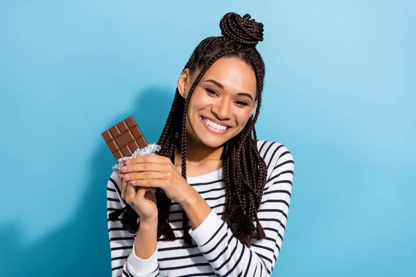 Foto de jovem atraente afro menina feliz positvie sorriso chocolate bar comida comer doce isolado sobre fundo de cor azul — Fotografia de Stock
