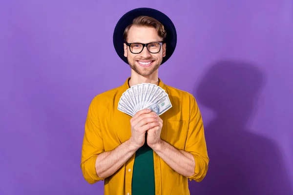 Retrato de atractivo chico alegre sosteniendo en las manos dólares en efectivo ventilador pasar aislado sobre violeta brillante color púrpura fondo — Foto de Stock