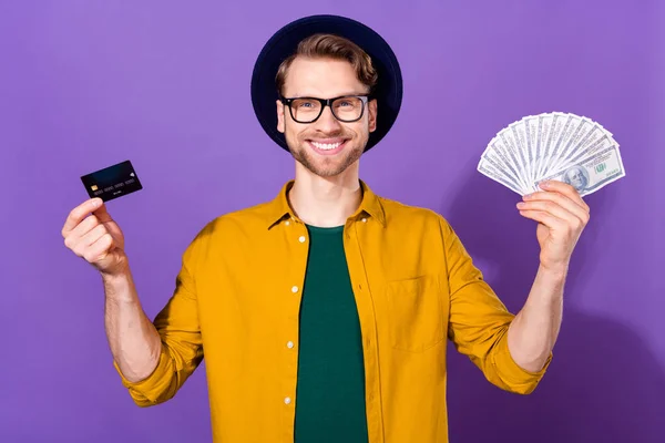 Photo of young guy happy positive smile hold cash money dollars bank card pay isolated over violet color background — Stockfoto