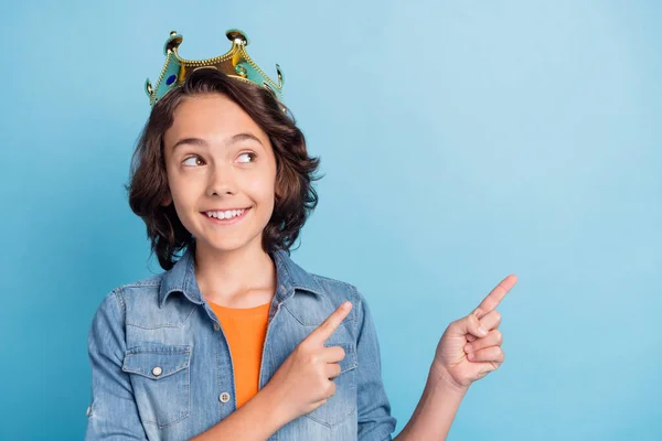Fénykép fiatal tizenéves fiú boldog pozitív mosoly korona herceg mutatóujj üres tér hirdetés választás elszigetelt felett kék színű háttér — Stock Fotó