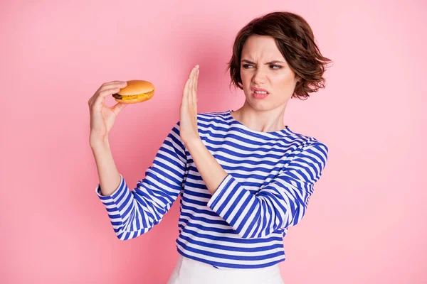 Retrato de joven atractiva chica negativa disgustada mira hamburguesa de la mano no negar aislado en el fondo de color rosa — Foto de Stock