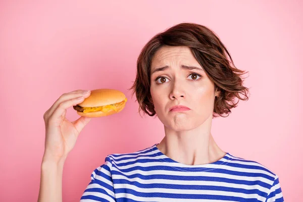 Retrato de joven hermosa molesto infeliz negativo estresado chica mantenga hamburguesa con queso aislado en el fondo de color rosa — Foto de Stock