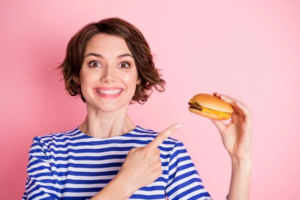 Portré fiatal eksztatikus vonzó vidám mosolygós lány ujjal mutogató sajtburger elszigetelt rózsaszín háttér — Stock Fotó