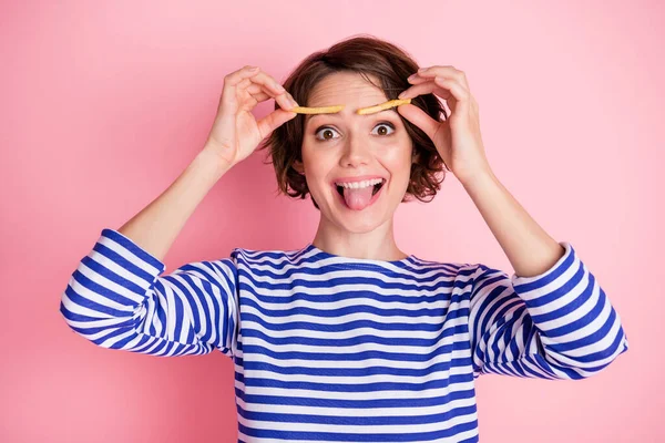 Retrato de la joven hermosa excitada chica funky palillo lengua hacia fuera mantenga papas fritas en las cejas aisladas en el fondo de color rosa —  Fotos de Stock