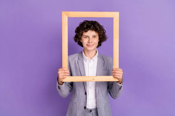 Foto de blogger positivo escolar sostiene marco de madera hacer retrato desgaste traje gris aislado color violeta fondo — Foto de Stock