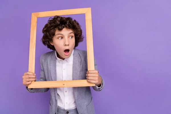 Foto de loco emocionado impactado pequeño chico mantenga marco mirada espacio vacío desgaste traje gris aislado violeta color fondo — Foto de Stock