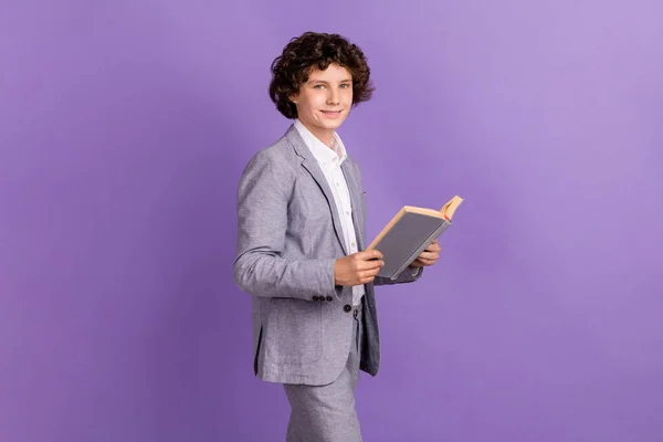 Foto di positivo piccolo ragazzo sedersi camminare tenere il libro di testo leggere usura abito grigio isolato colore viola sfondo — Foto Stock