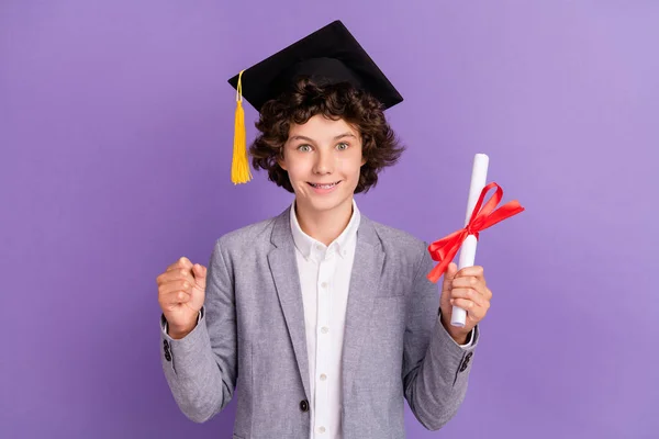 Fotografie veselý pozitivní školák držet diplom promoce vyhrát nosit klobouk šedý oblek izolované fialové barvy pozadí — Stock fotografie