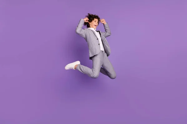 Profilbilde av sprø skolegutt hoppe feire seier bære grå dress isolert fiolett bakgrunn – stockfoto