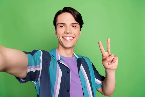 Zdjęcie funky brunet młody facet do selfie show v-sign nosić niebieską koszulę izolowane na zielonym tle kolor — Zdjęcie stockowe