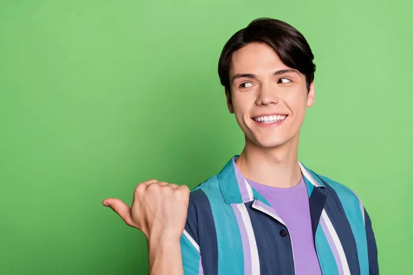Photo of funny brunet young guy point look space wear blue shirt isolated on green color background — Stock Photo, Image