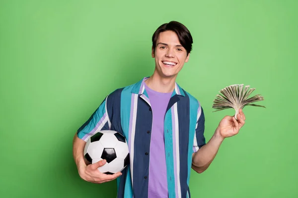 Foto de alegre jovem feliz homem positivo segurar mãos dinheiro futebol aposta isolada no fundo de cor verde — Fotografia de Stock