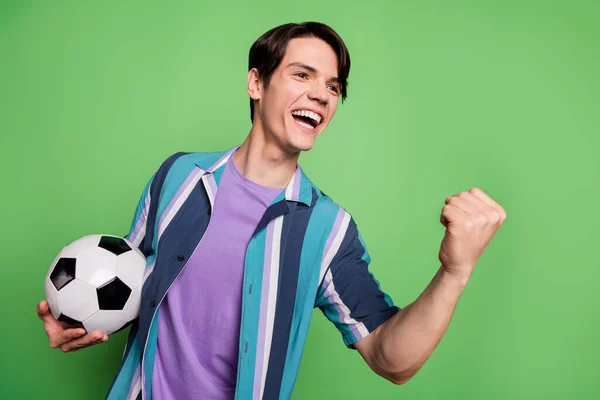Фото позитивного молодого веселого человека поднять кулак провести футбольный победитель праздновать изолированы на зеленом фоне — стоковое фото