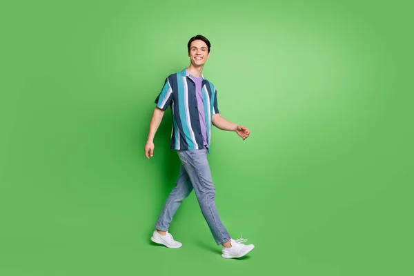 Full length photo of charming happy young man walk empty space good mood weekend isolated on green color background — ストック写真