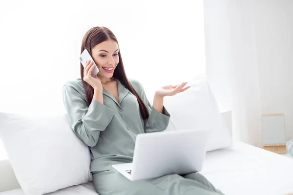 Full size corpo foto donna seduta sul letto di lavoro sul computer portatile parlando sul cellulare — Foto Stock