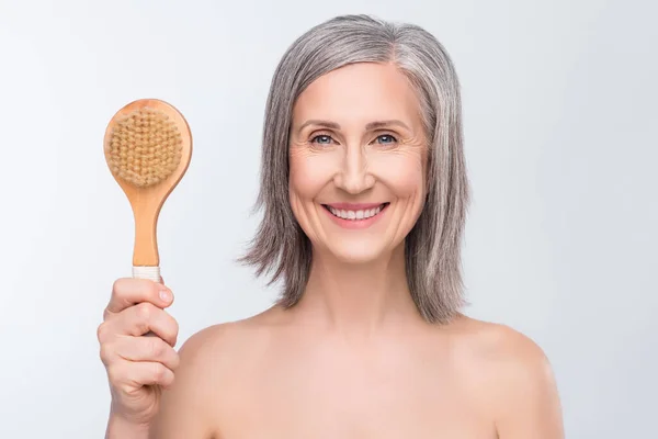 Photo of attractive charming nice old woman hold had wooden brush smile massage isolated on grey color background — ストック写真