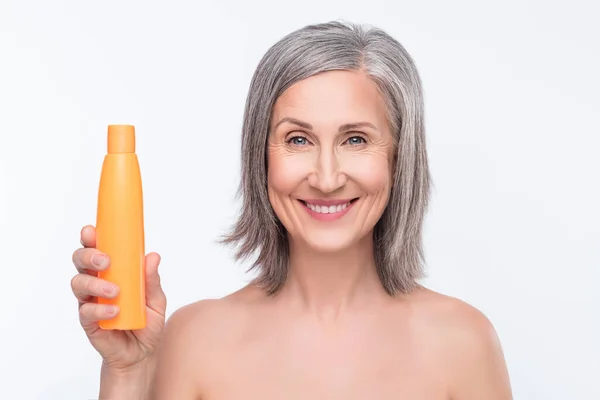 Foto de uma mulher idosa alegre positiva sorrir bom humor segurar garrafa loção higiene isolada no fundo de cor cinza — Fotografia de Stock