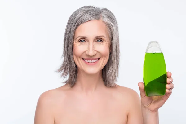 Foto de encantador positivo mulher velha segurar mão garrafa shampoo cuidados corpo isolado no fundo de cor cinza — Fotografia de Stock