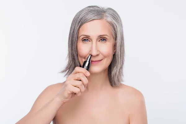 Photo of charming white haired old woman use electric shave nose machine isolated on grey color background — ストック写真