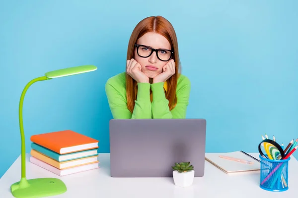 Retrato de la atractiva chica triste y malhumorada usando el ordenador portátil haciendo aburrida tarea aislada sobre fondo de color azul pastel —  Fotos de Stock