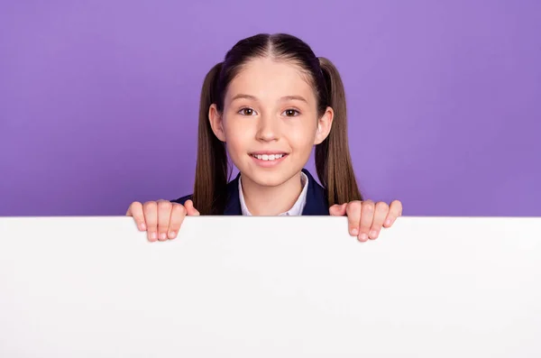 Foto de encantadora colegiala bonita vestida azul uniforme sonriente sosteniendo brazos letrero blanco espacio vacío aislado color violeta fondo —  Fotos de Stock