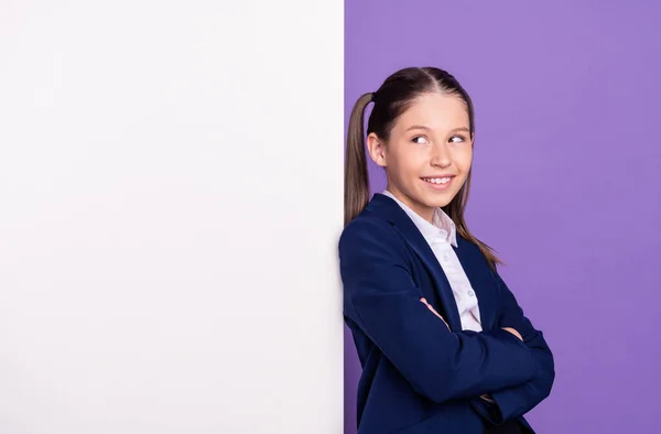 Foto de encantadora chica divertida de la escuela usar brazos uniformes azules plegados buscando cartelera blanca espacio vacío aislado color púrpura fondo —  Fotos de Stock