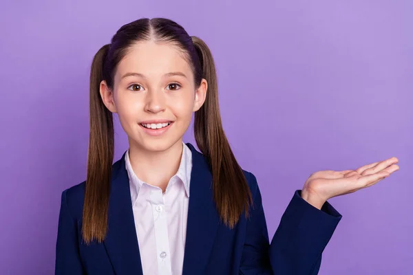 Foto de bonito encantador escola menina desgaste azul uniforme segurando braço vazio espaço sorrindo isolado roxo cor fundo — Fotografia de Stock