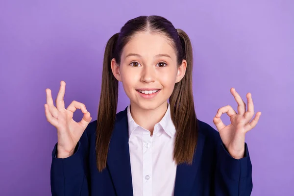 Foto de bom humor menina da escola alegre desgaste azul uniforme sorrindo mostrando okey sinais isolado cor roxa fundo — Fotografia de Stock