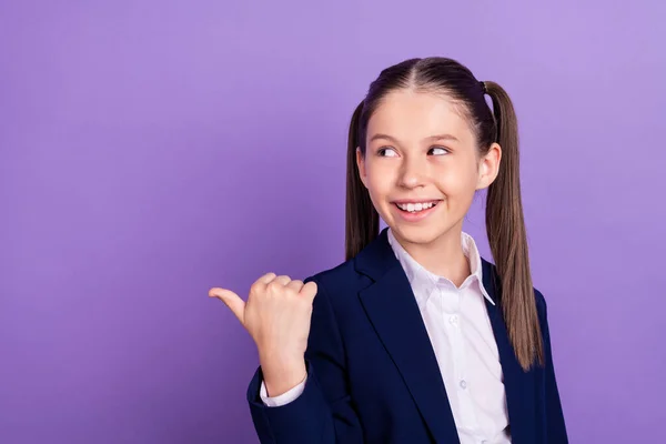 Zdjęcie śmieszne słodkie dziewczyny szkoły nosić niebieski mundur patrząc wskazując kciuk puste miejsce uśmiechając się odizolowany fioletowy kolor tła — Zdjęcie stockowe