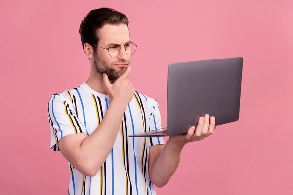 Фото мыслящего молодого человека смотреть ноутбук носить очки бизнесмен изолирован на пастельно-розовый цвет фона — стоковое фото