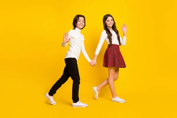 Plná délka tělo velikost boční profil fotografie dětí drží ruce jít do školy mávání ruce izolované zářivé žluté barvy pozadí — Stock fotografie