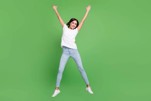 Full length photo of funny brunette young lady jump wear t-shirt jeans isolated on green color background — Stock Photo, Image