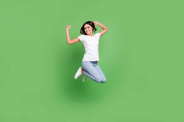 Full body photo of funky brunette young lady jump wear t-shirt jeans isolated on green color background — Stock Photo, Image