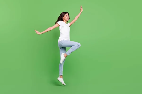 Full length profile photo of nice brunette millennial lady jump wear t-shirt jeans isolated on green color background — Stock Photo, Image