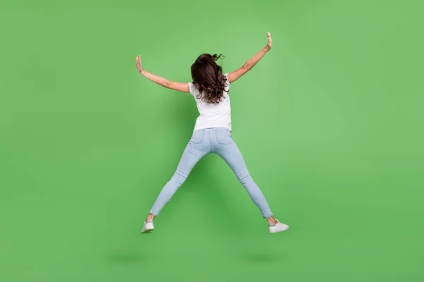 Full body back photo of cool brunette young lady jump wear t-shirt jeans isolated on green color background — Stock Photo, Image