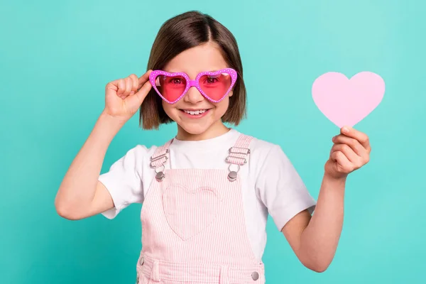 Foto de doce colegial bonita vestida rosa óculos braço geral segurando papel coração sorrindo isolado cor turquesa fundo — Fotografia de Stock