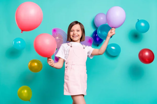 Foto van charmante grappige school meisje dragen roze algemene vleugels glimlachen spelen ballonnen geïsoleerde teal kleur achtergrond — Stockfoto