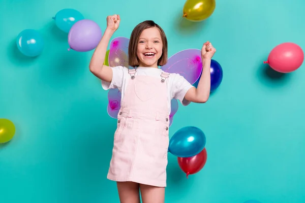 Foto van zoet geluk schoolmeisje gekleed roze overall vleugels rijzende vuisten kleurrijke ballonnen geïsoleerde turquoise kleur achtergrond — Stockfoto