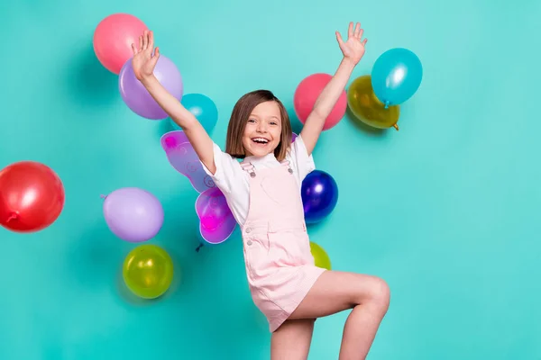 Foto di divertente adorabile ragazza della scuola indossare le ali complessive rosa sorridente giocare palloncini ascendente braccia isolato colore verde acqua sfondo — Foto Stock