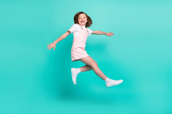 Фото впечатленной сладкой школьницы одета розовый общий прыжки высокий улыбаясь изолированный бирюзовый цвет фона — стоковое фото
