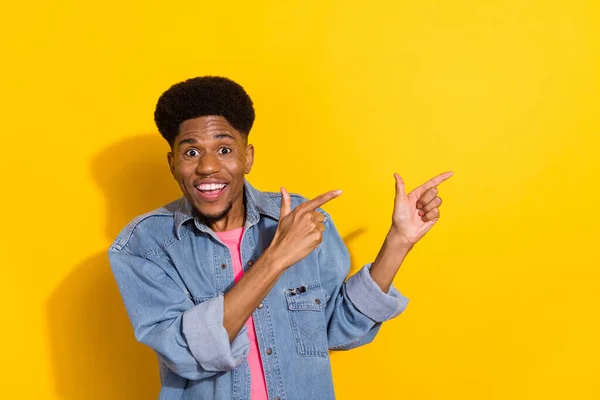 Foto de alegre joven piel oscura hombre positivo dedo dedo vacío espacio noticias aisladas en el fondo de color amarillo —  Fotos de Stock