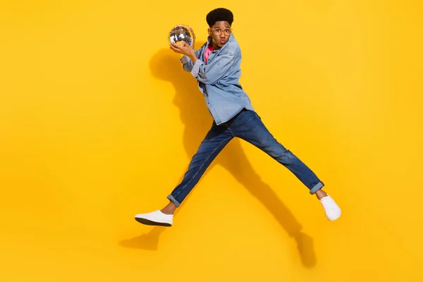 Foto em tamanho completo do homem afro-americano salto desgaste jeans camisa segurar bola disco enviar beijo de ar isolado no fundo de cor amarela — Fotografia de Stock