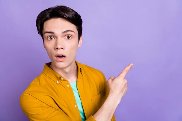 Foto van onder de indruk brunet jonge man punt lege ruimte dragen geel shirt geïsoleerd op violette kleur achtergrond — Stockfoto