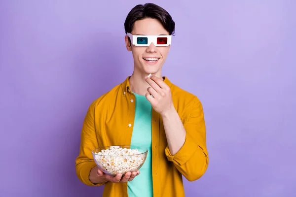 Photo of funky brunet millennial guy eat popcorn wear spectacles yellow shirt isolated on violet color background — Stock Photo, Image