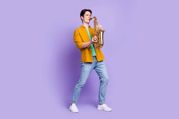 Foto de comprimento total de cara milenar morena agradável jogar saxofone desgaste camisa jeans isolado no fundo cor violeta — Fotografia de Stock