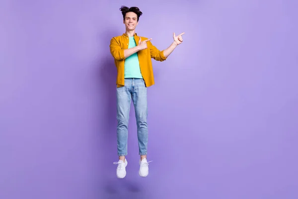 Foto em tamanho completo de bom morena millennial cara ponto de salto espaço vazio desgaste camisa jeans isolado no fundo cor violeta — Fotografia de Stock