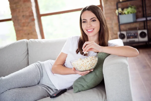 Фото молодой привлекательной девушки счастливая положительная улыбка лежа диван смотреть кино комедия едят поп-кукурузу в помещении — стоковое фото