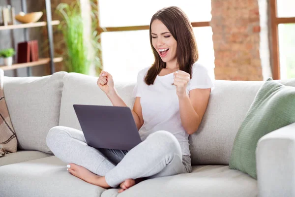 Foto retrato morena mujer sentada en el sofá en casa trabajando en el gesto de la computadora como ganador — Foto de Stock